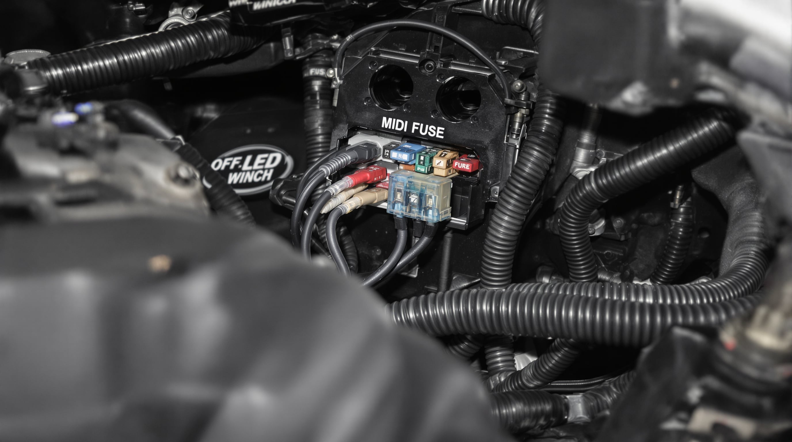 Photograph of an engine bay showing a midi auto fuse with thick cables connected to high-power accessories like a winch and LED light bar.