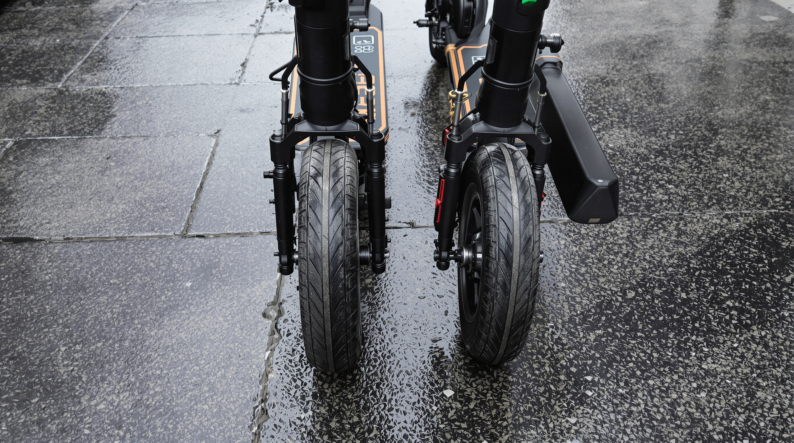 Side-by-side scooters on wet pavement showing puncture-proof versus pneumatic tires for performance comparison.