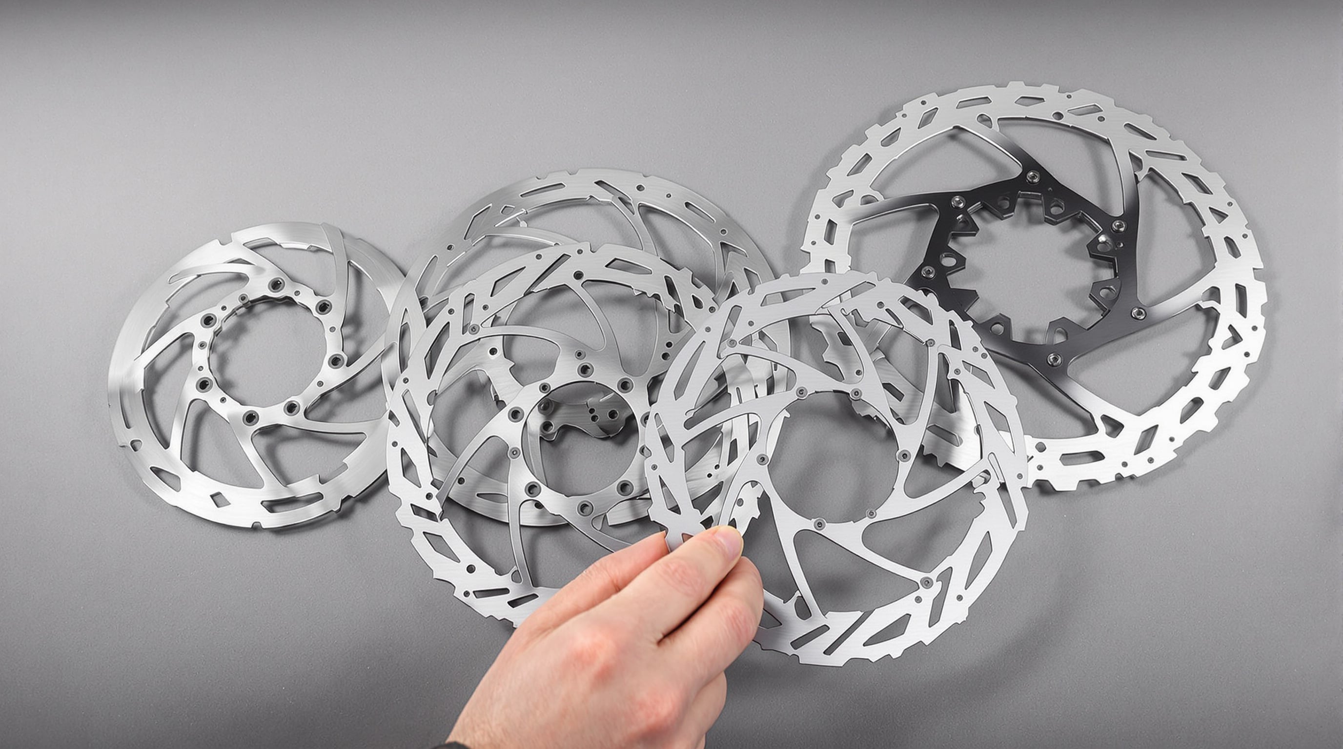 Assorted sizes of e-bike disc brake rotors displayed on a workbench with a hand reaching for the largest one