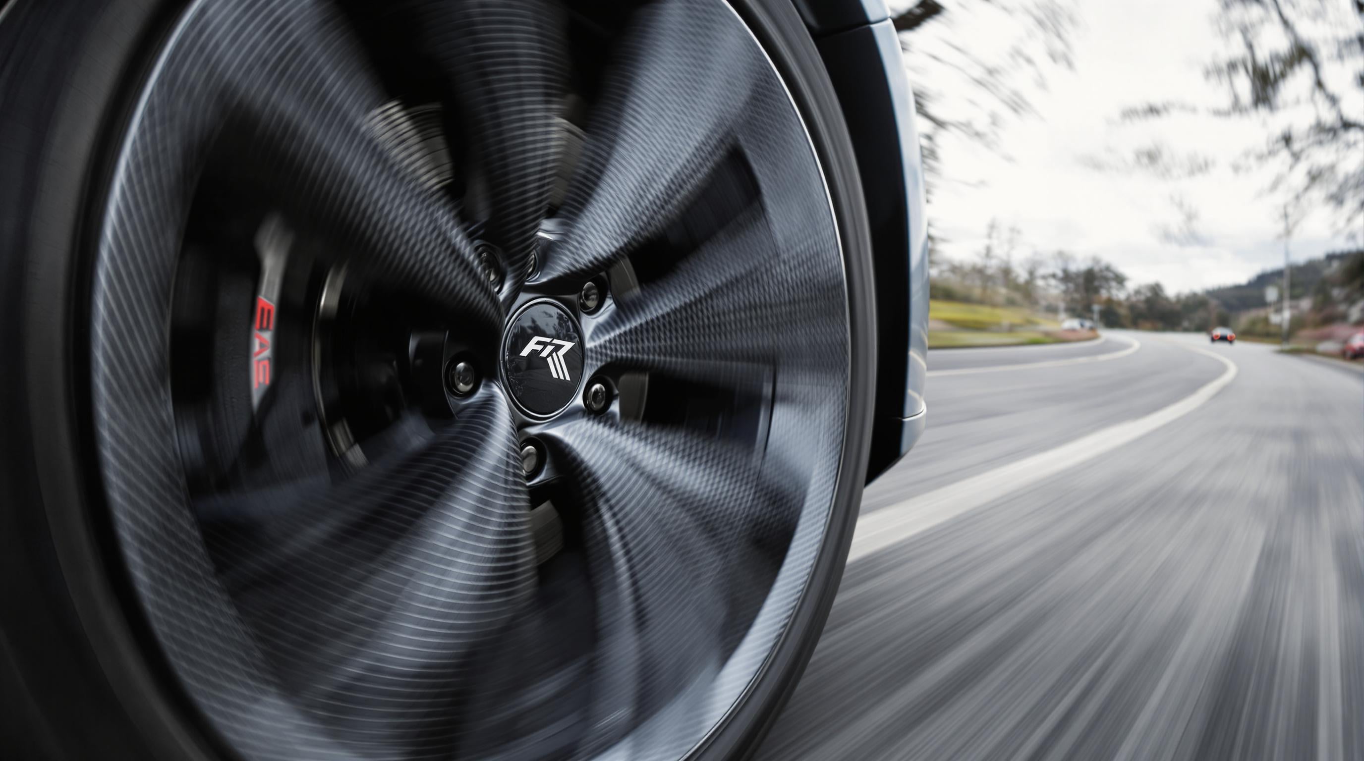 Close-up photo of a carbon fiber car wheel spinning on a road, emphasizing detail and motion