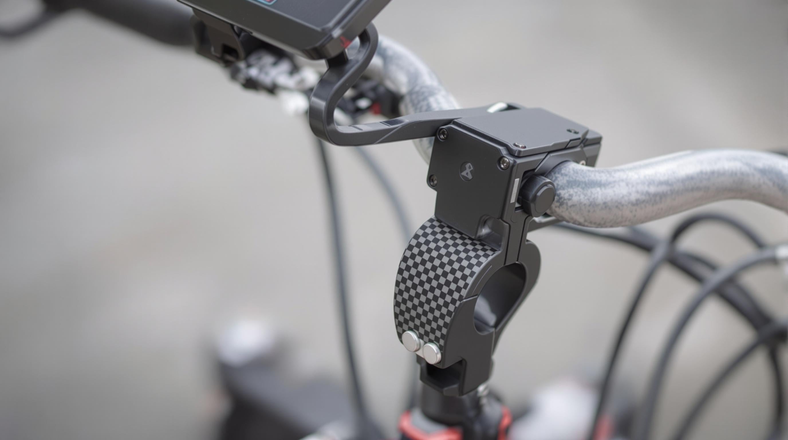 A photorealistic close-up of a dual-use selfie stick clamp mounted on bicycle and motorcycle handlebars, highlighting silicone grips and secure lock features.