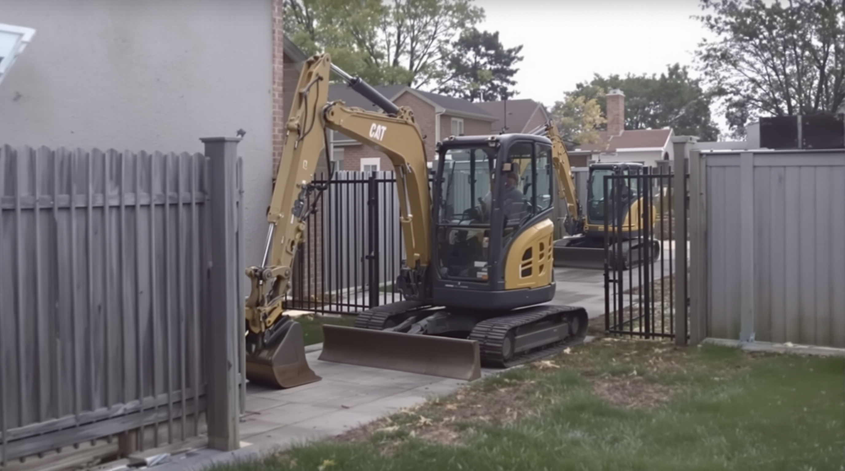 A compact mini excavator fitting through a narrow backyard gate while a larger excavator is visible outside.