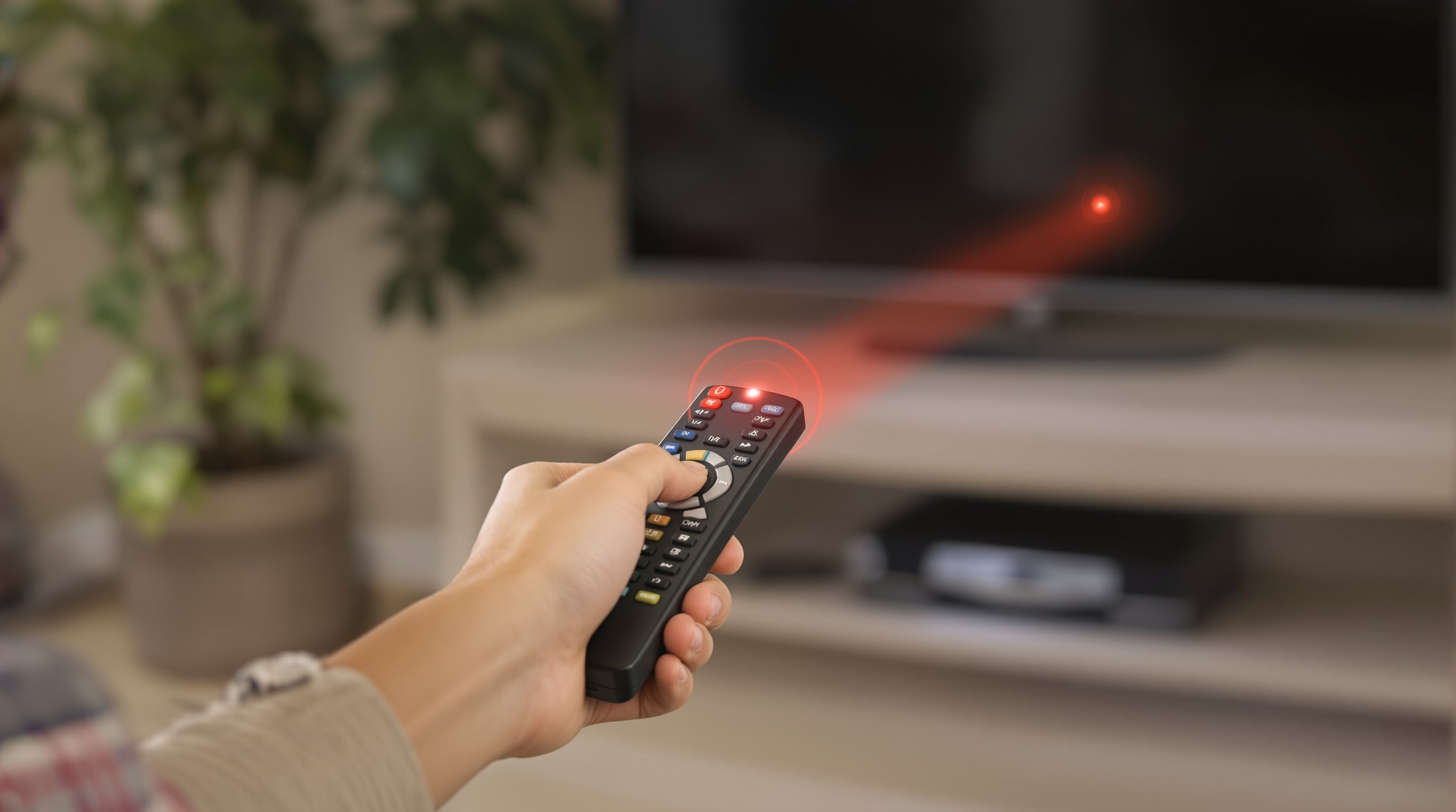 Person using an infrared remote aimed at a TV in a living room, showing need for line of sight
