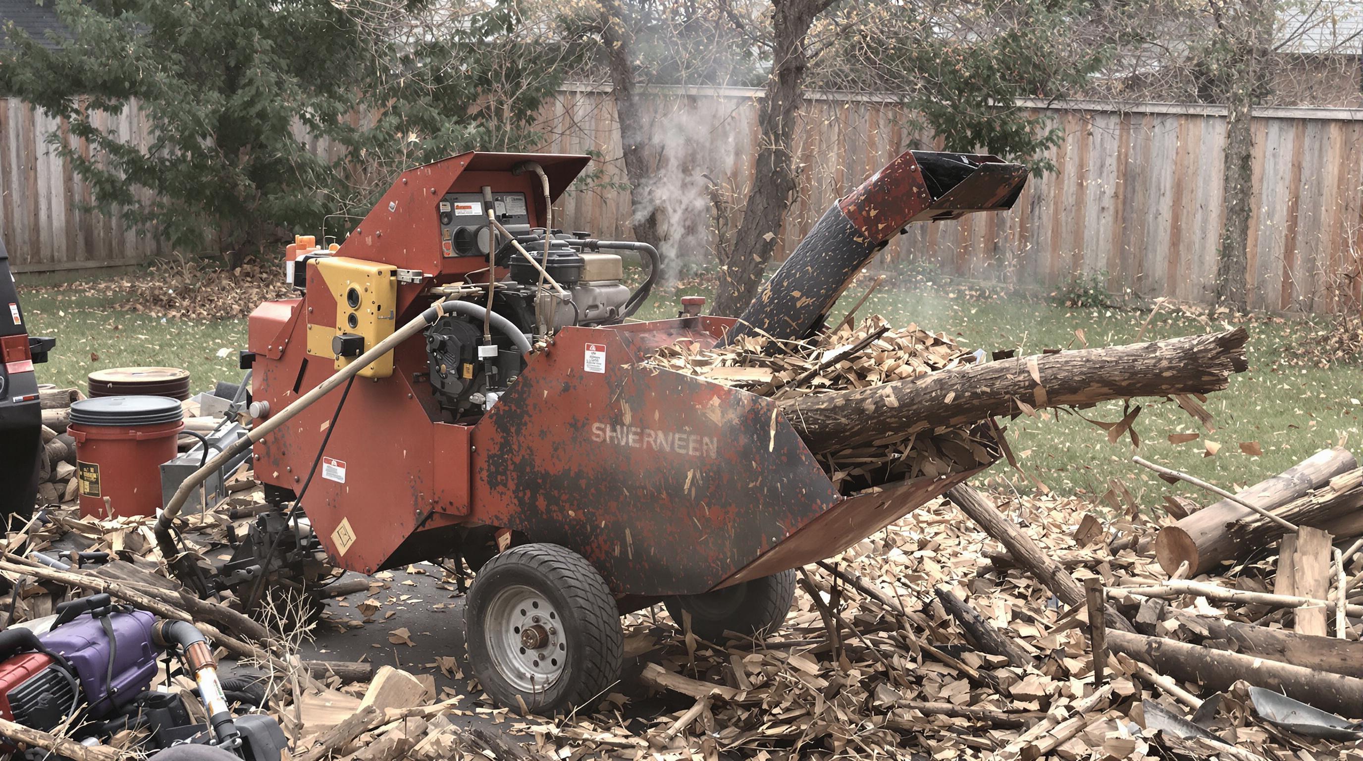 An older chipper shredder in a backyard having difficulty processing a branch, with an operator nearby and wood debris piling up