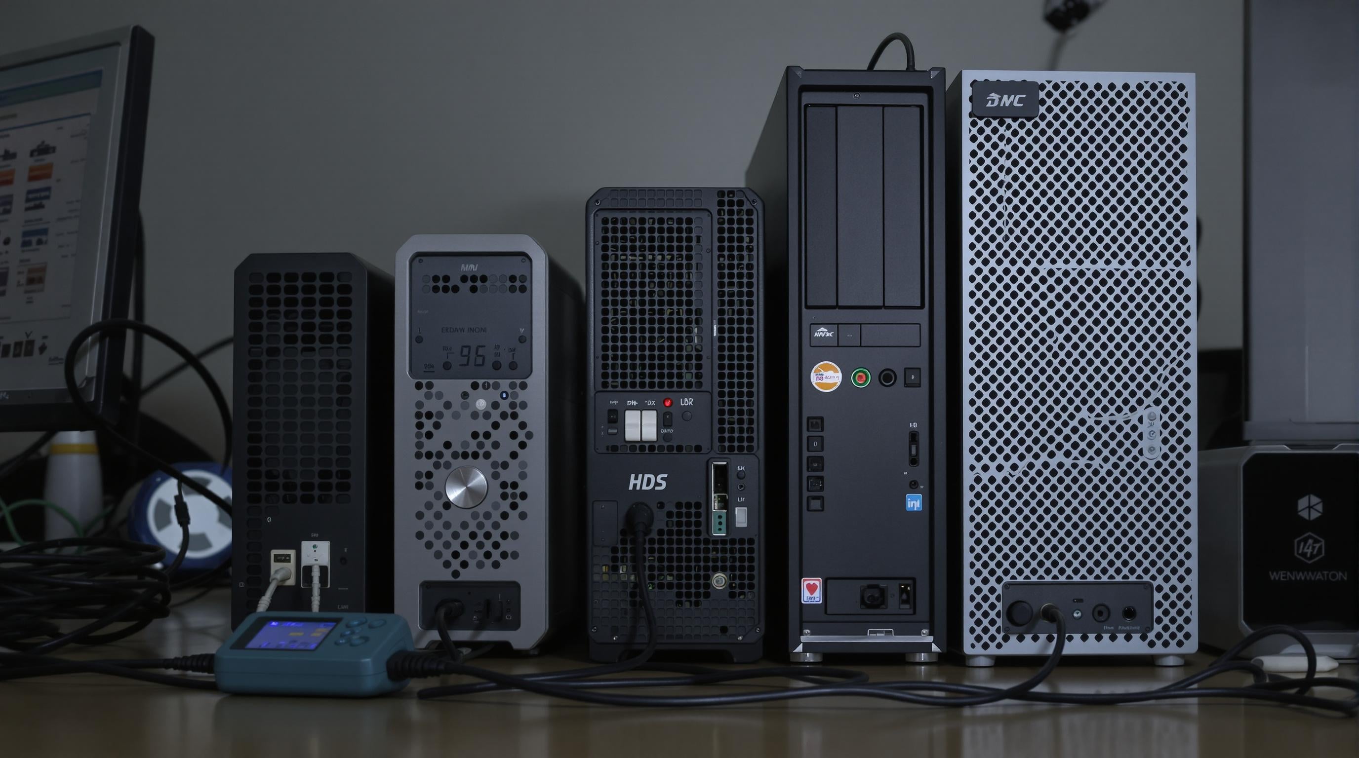 Photo showing mini PCs next to a traditional desktop computer on a desk, with energy meters and cables highlighting power use differences.