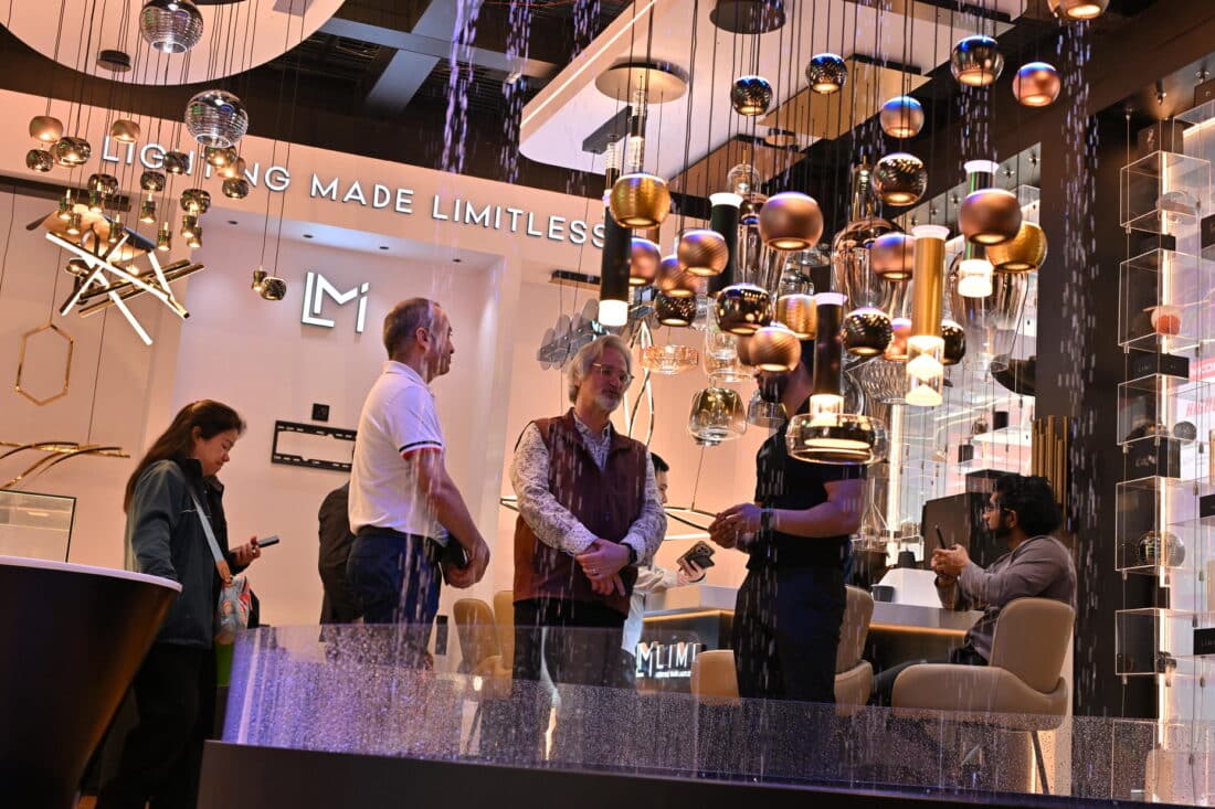 Lighting exhibition booth with professionals discussing aluminum frame applications under modern suspended lights, featuring diverse geometric fixtures and a bold 'LIGHTING MADE LIMITLESS' wall slogan emphasizing innovative material solutions for commercial lighting systems.