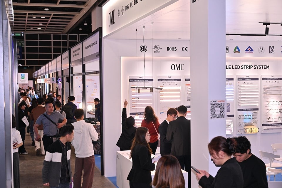 Busy exhibition hall at international lighting trade show with attendees discussing technical specifications, white booths displaying ROHS/CE certified electronic components and aluminum profile applications, blue floor guides directing foot traffic under bright industrial lighting.