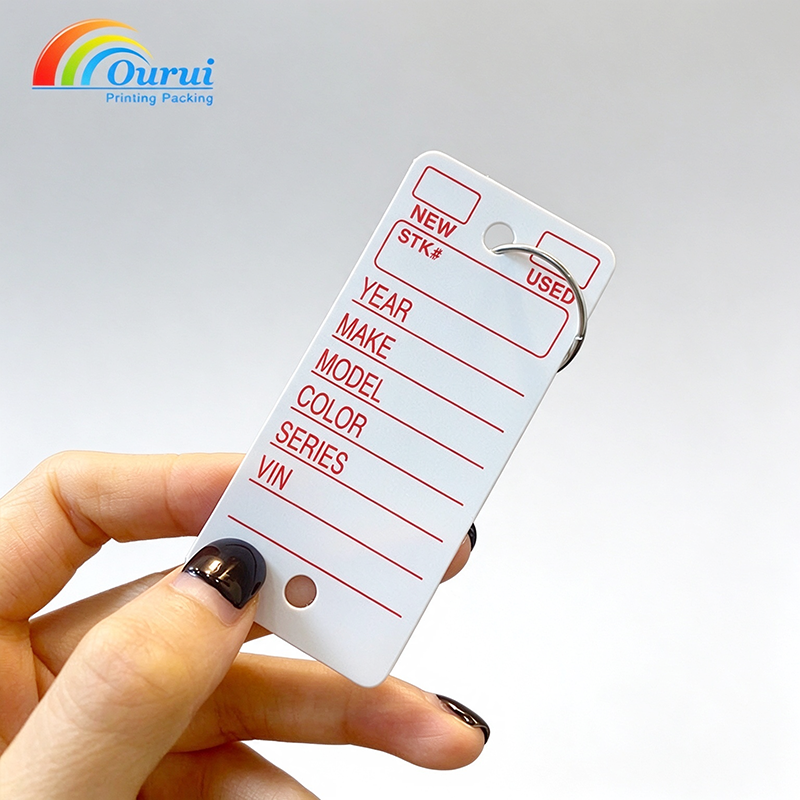 White printed auto key tag with red printed Year Make Model VIN form, hand closeup(7a5e20f659).png