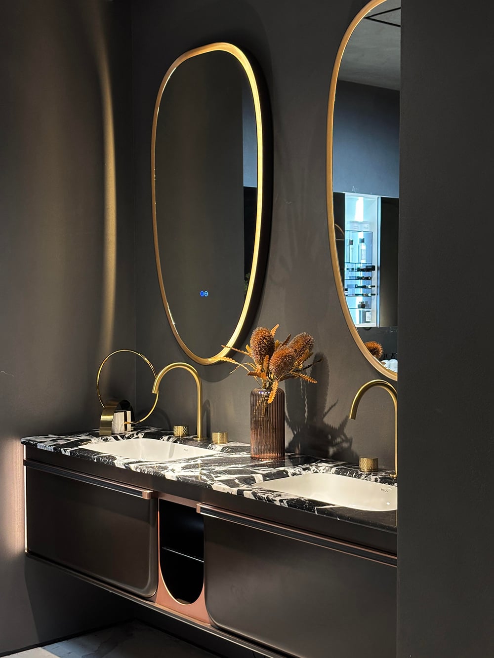 Mobile bagno di lusso per hotel con piano in marmo nero, specchi ovali con dettagli dorati e vani contenitori moderni per uno spazio bagno sofisticato