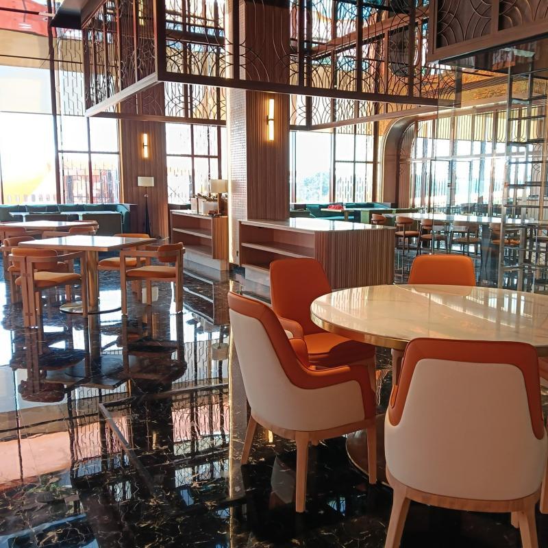 Hotel dining room area with round wooden top tables and orange padded commercial dining chairs.webp