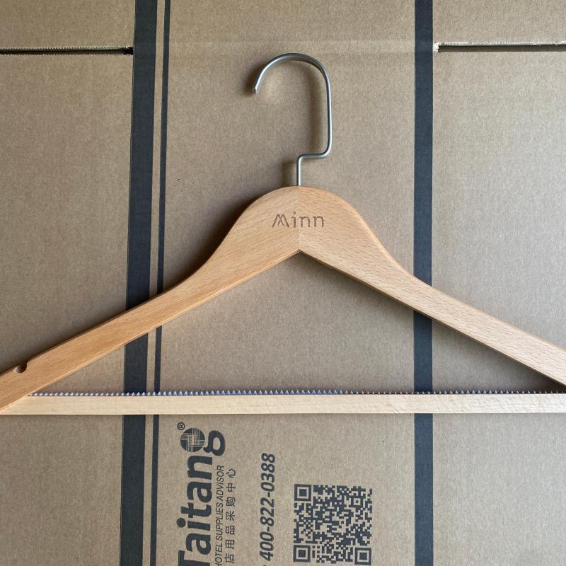 Solid wood hotel coat hanger with custom engraved logo resting on a Taitang export carton.JPG