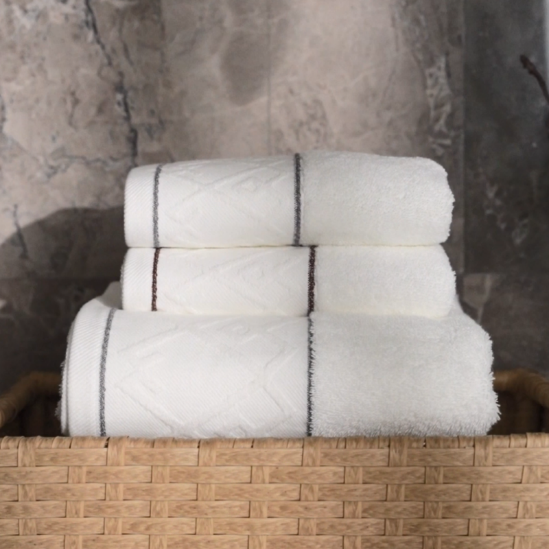 Stack of premium white luxury hotel towels with grey embroidered borders presented in a woven basket by Taitang.png