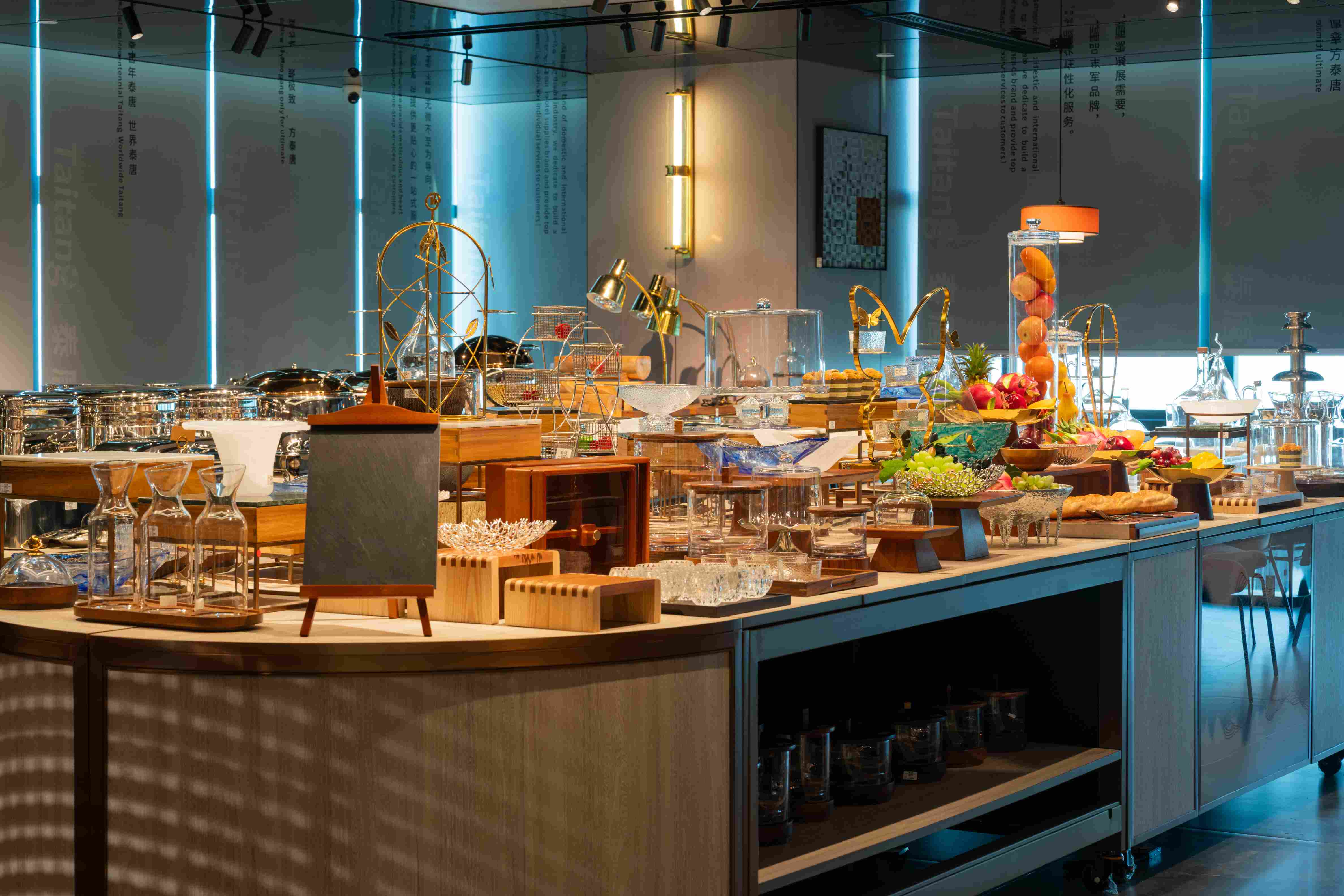 An elegantly arranged buffet table or presentation area with glass cloches, wooden stands, glassware, fruit arrangements, and professional servingware.