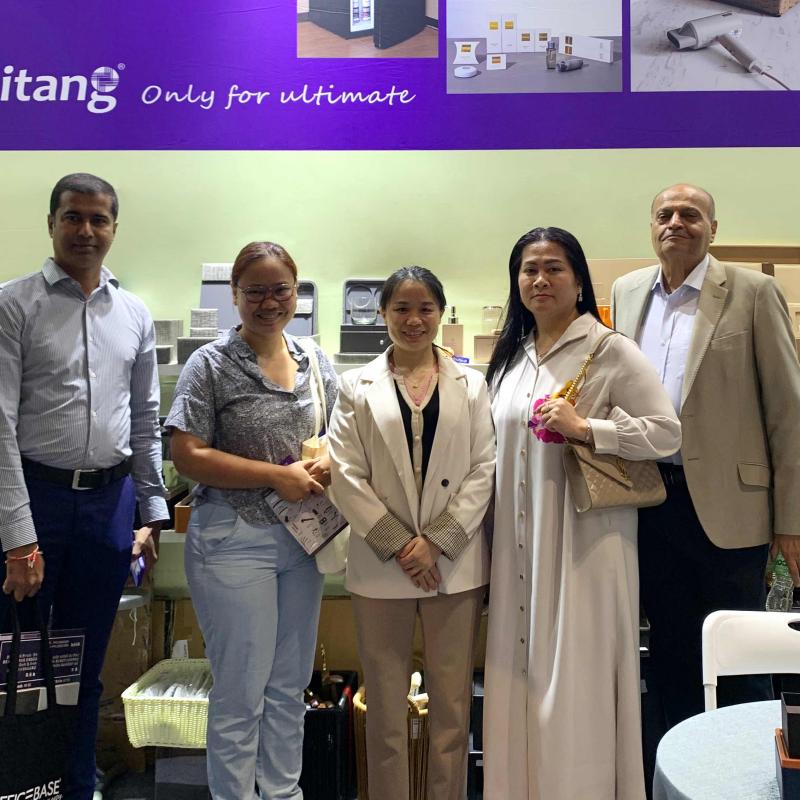 Taitang team members posing for a group photo with international visitors inside their purple-branded trade show booth at the Dubai hotel supplies exhibition.jpg