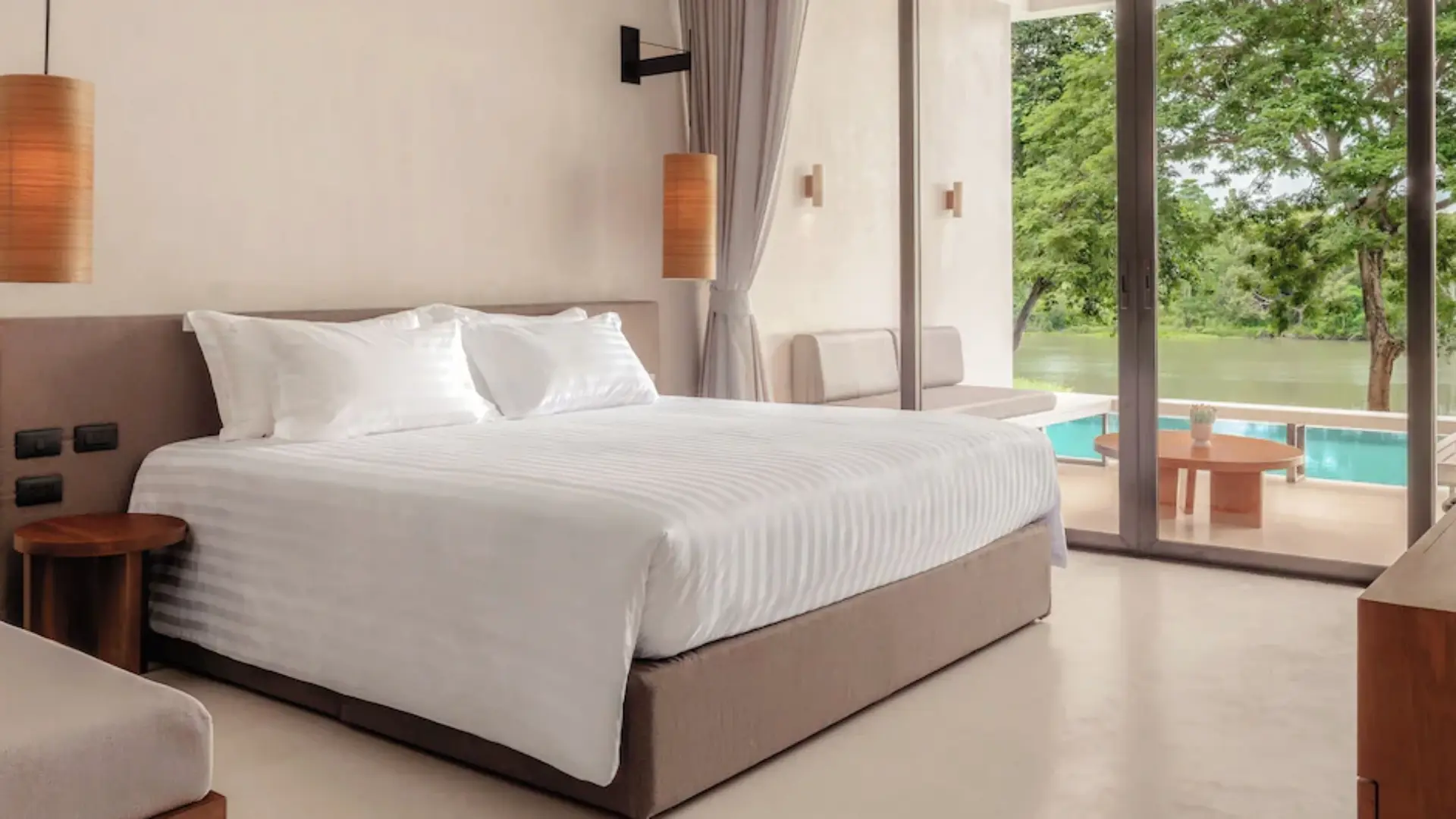 Resort suite bedroom featuring crisp white bed linens and floor-to-ceiling river view terrace windows.webp