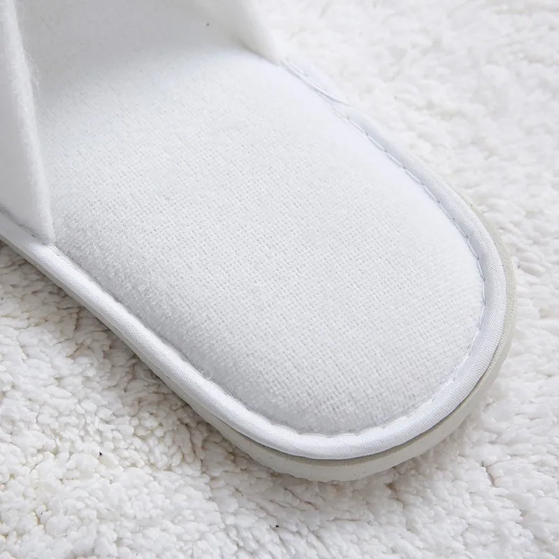 The top view of a white hotel slipper on a plush white carpet.