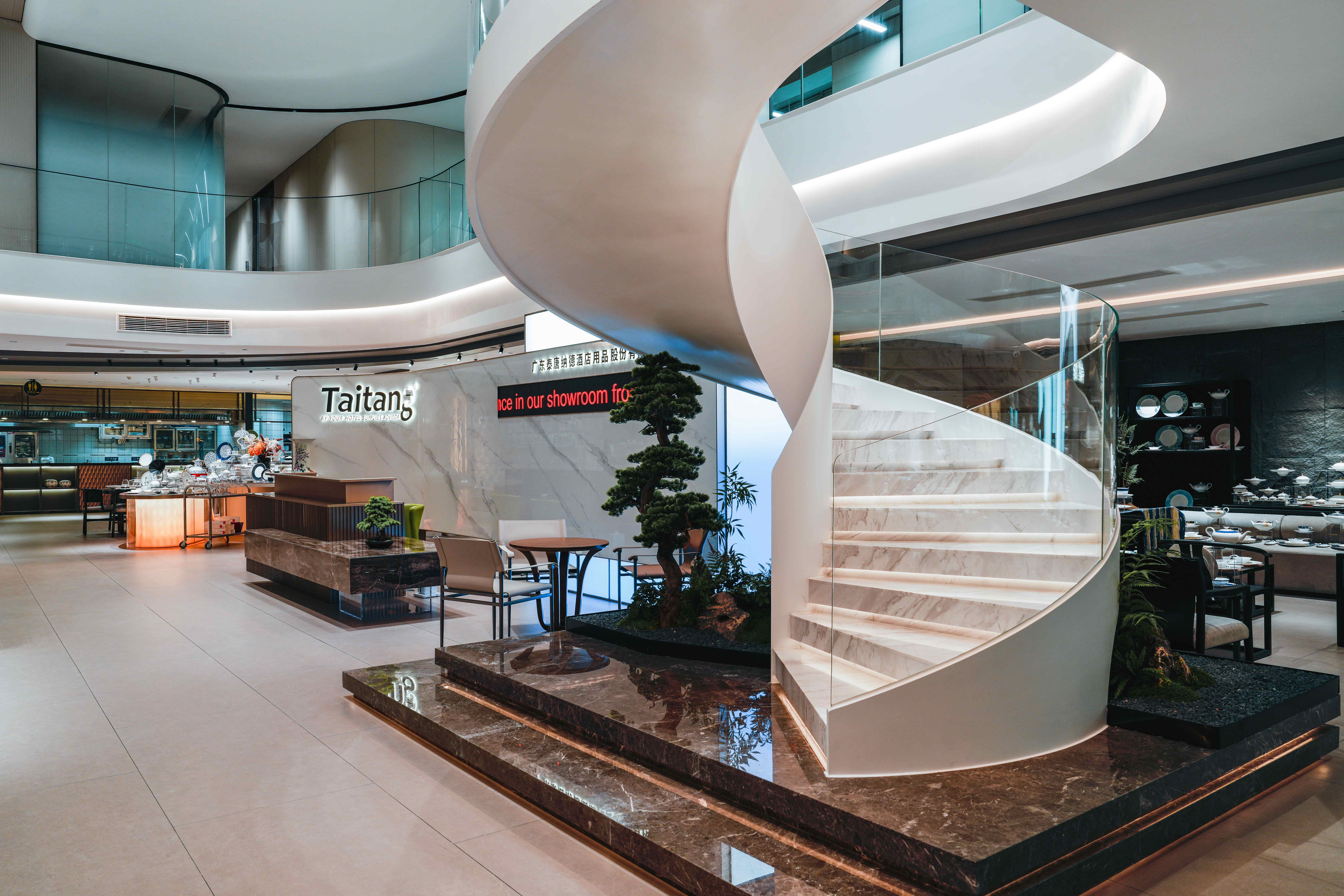 A luxurious and modern Taitang hotel supplies showroom, featuring an elegant marble reception counter with the official 'Taitang' logo, a sleek winding staircase, and comprehensive product displays, positioned as a leading comprehensive hotel OS&E provider for the hospitality industry.