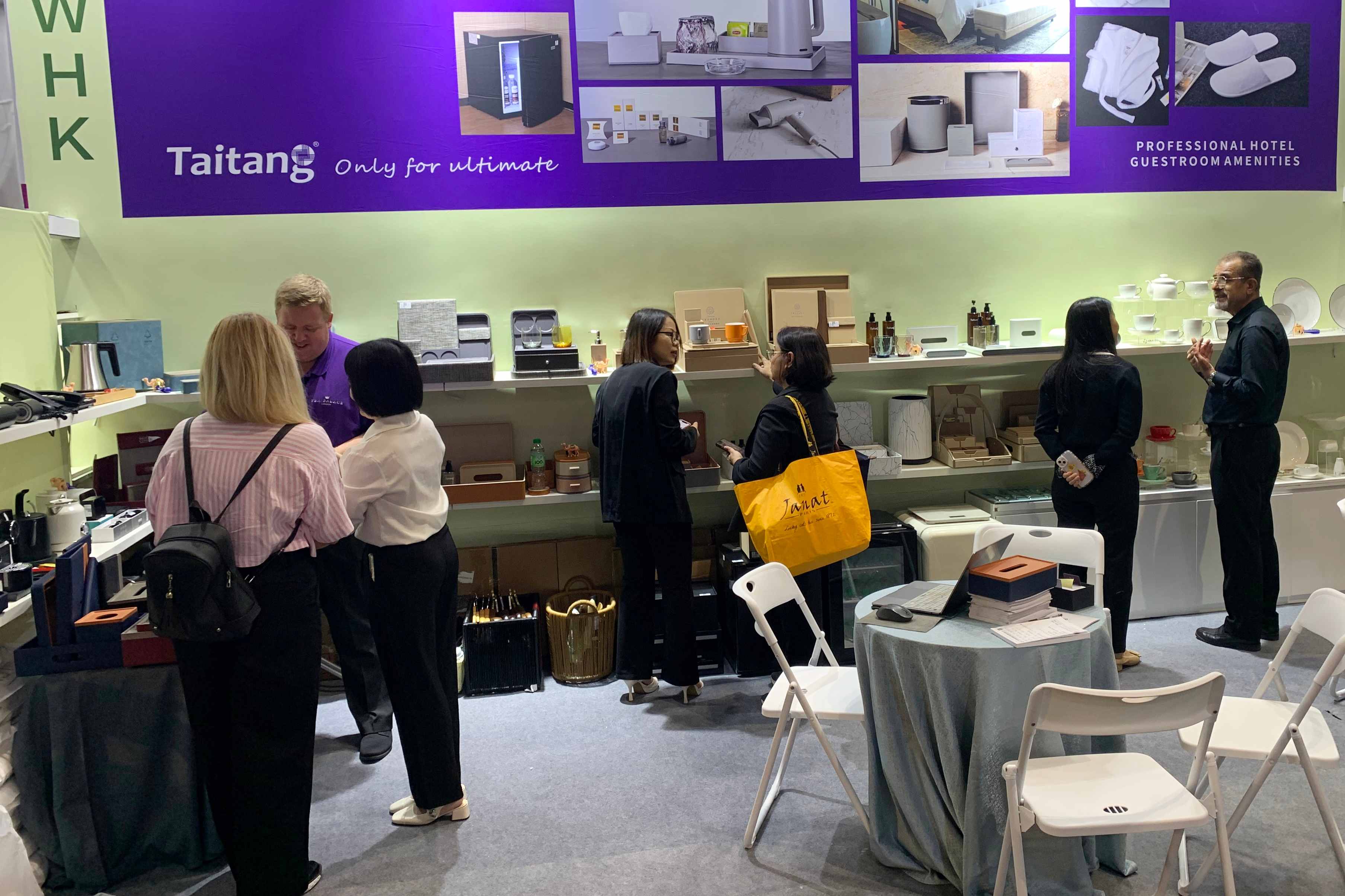 An overview of the TAITANG booth at an international trade fair, featuring various hotel room supplies and a professional consultation area.