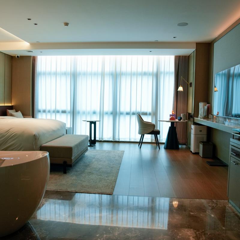 A panoramic view of a simulated luxury hotel guest room interior designed by Taitang, showing a complete bed, a lounge chair, and a bathtub setup.JPG