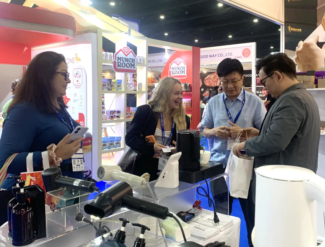 International hotel procurement managers discussing customized coffee machines and electric kettles with Taitang representatives at the Bangkok trade show.