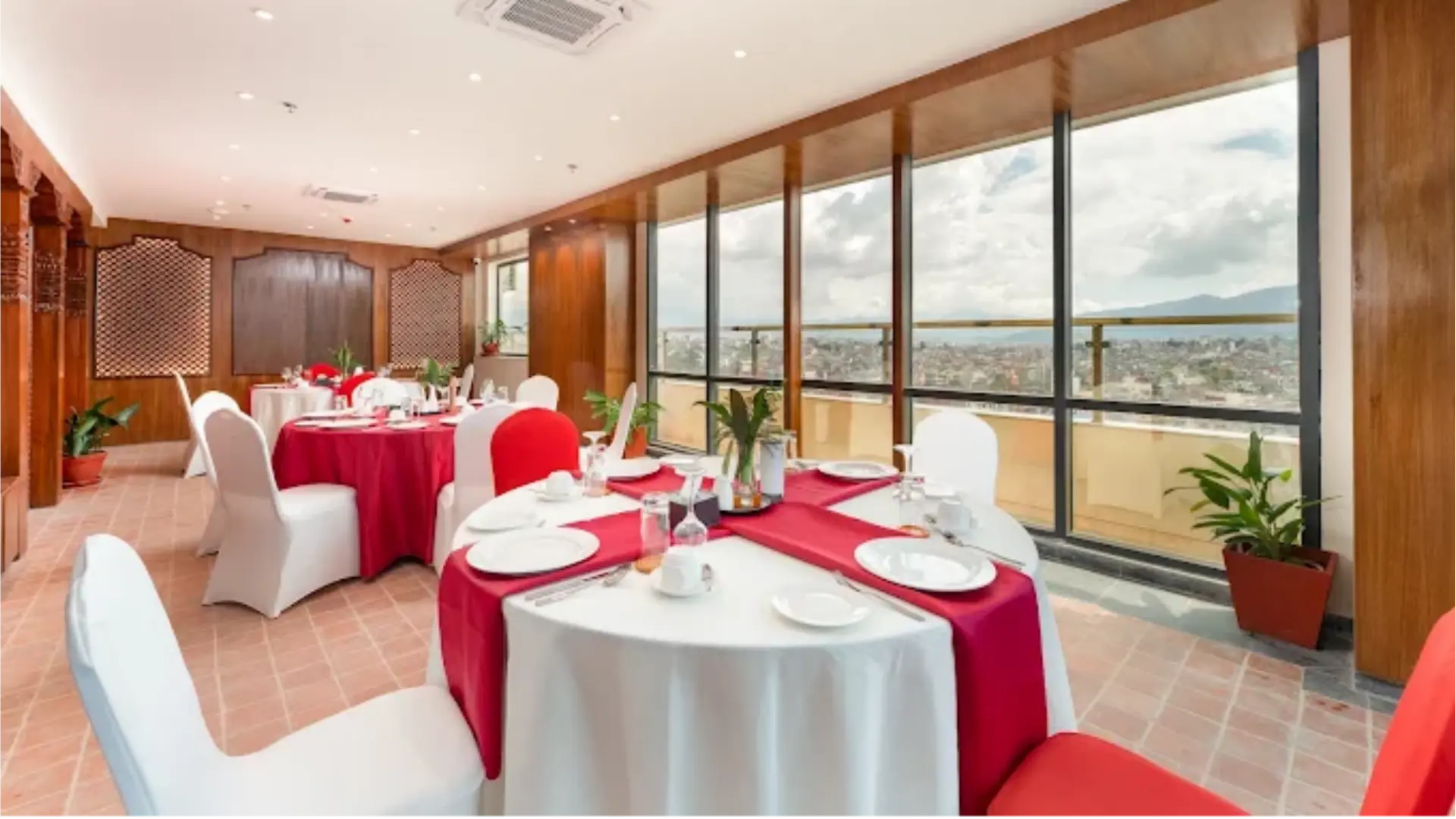 Hotel banquet hall dining setup featuring round tables draped in red and white tablecloths.webp
