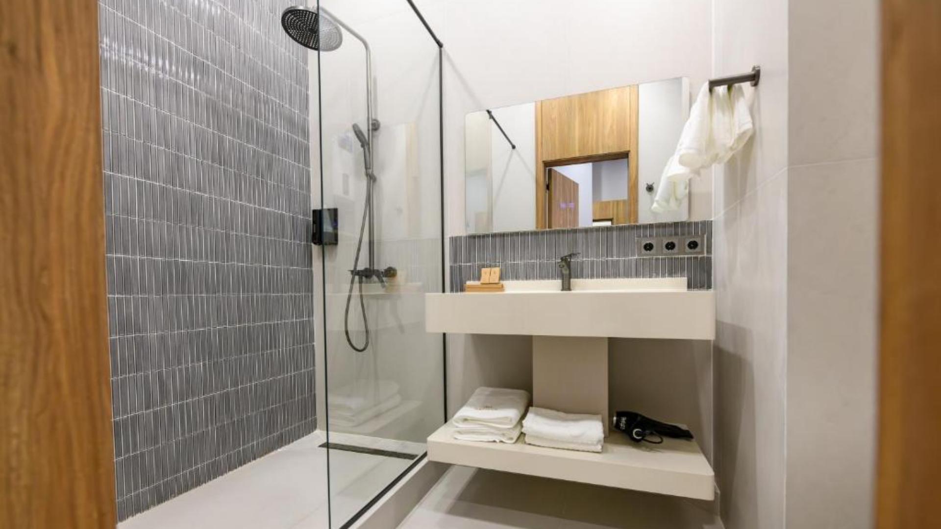 Modern hotel bathroom setup with walk-in glass shower, vanity mirror, and neatly stacked white bath towels.jpg