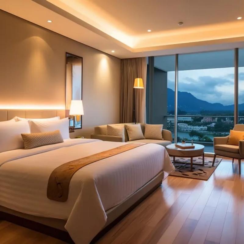 Modern hotel suite bedroom with warm ambient lighting, large windows, sofa seating area, and a neatly made bed.jpg