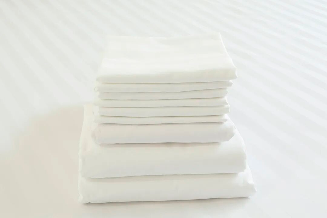 A neat stack of folded white hotel towels and sheets, representing operational efficiency and the ability of white cotton to withstand high-temperature disinfection.