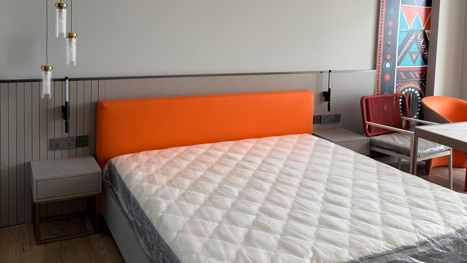 Modern resort guestroom featuring a king bed with vibrant orange upholstered headboard and custom side tables.jpg