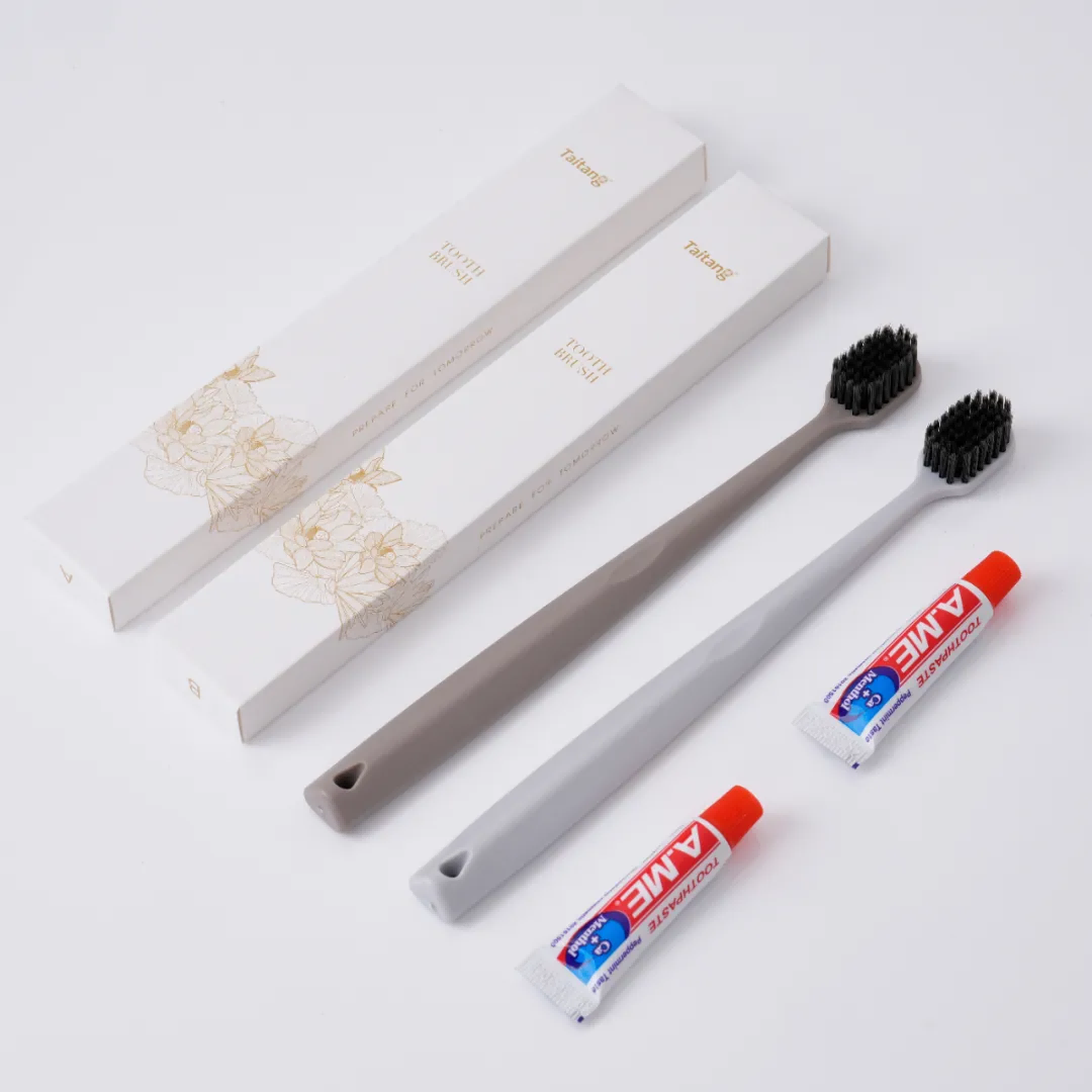 Hotel amenity kit featuring two toothbrushes with matte grey handles and black bristles, three small boxes, and two tubes of toothpaste.