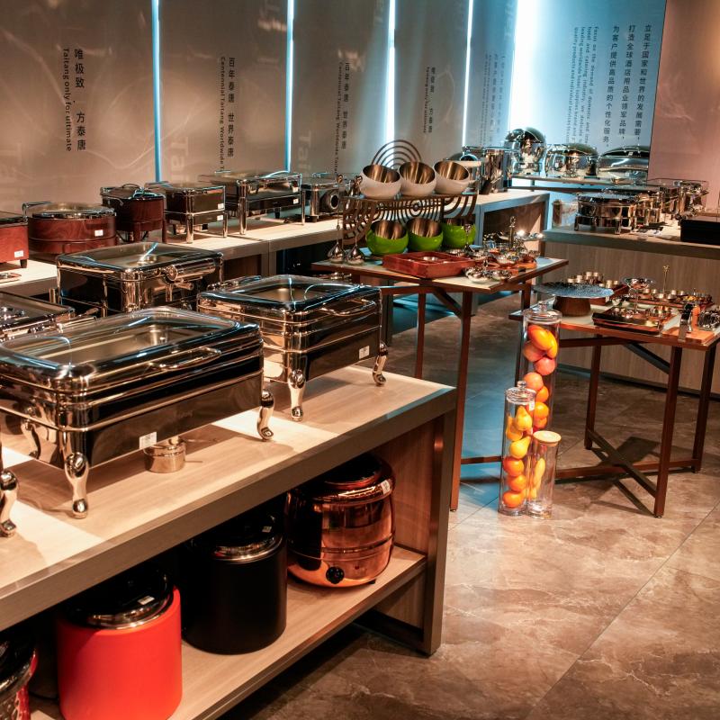 Detailed shot focusing on stainless steel rectangular chafer dishes with glass lids, elevated on custom stands, integrated with fruit bowls on a professional marble counter by Taitang.JPG