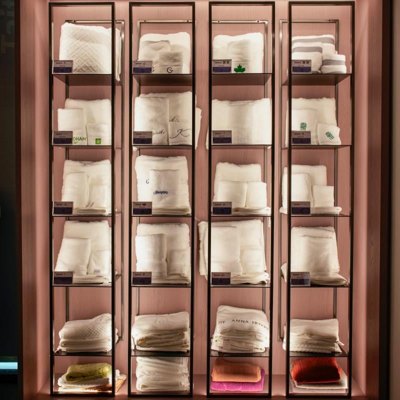 Taitang wholesale luxury hotel bath towels and non-slip bath mats organized on illuminated display shelves for hospitality procurement.JPG