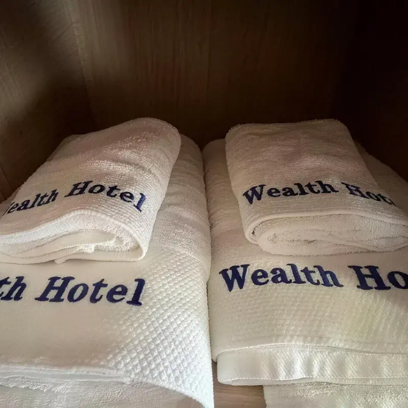 Custom embroidered white hotel bath towels featuring navy blue Wealth Hotel logo embroidery.webp