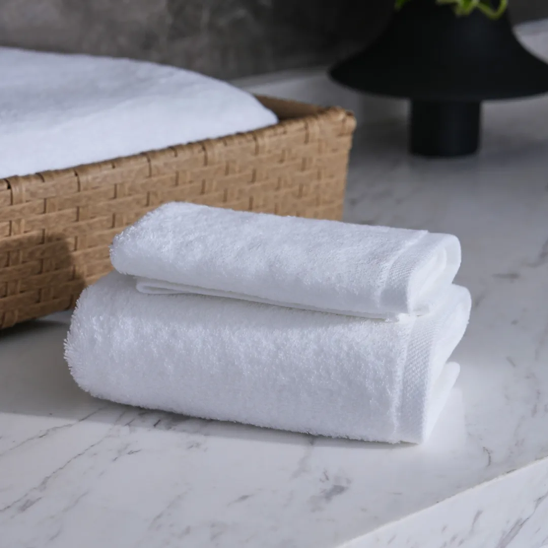 A stack of clean white hotel towels in a light-colored woven basket on a marble surface, next to a black table.