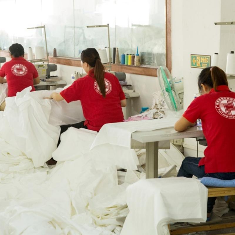 Factory workers in red uniforms stitching white hotel linens and duvets during manufacturing.jpg