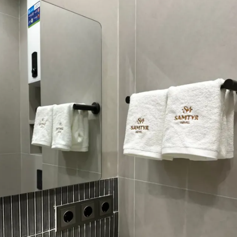 Plush white hotel bath towels customized with golden SAMTYR logo embroidery hanging on modern black bathroom towel racks.png