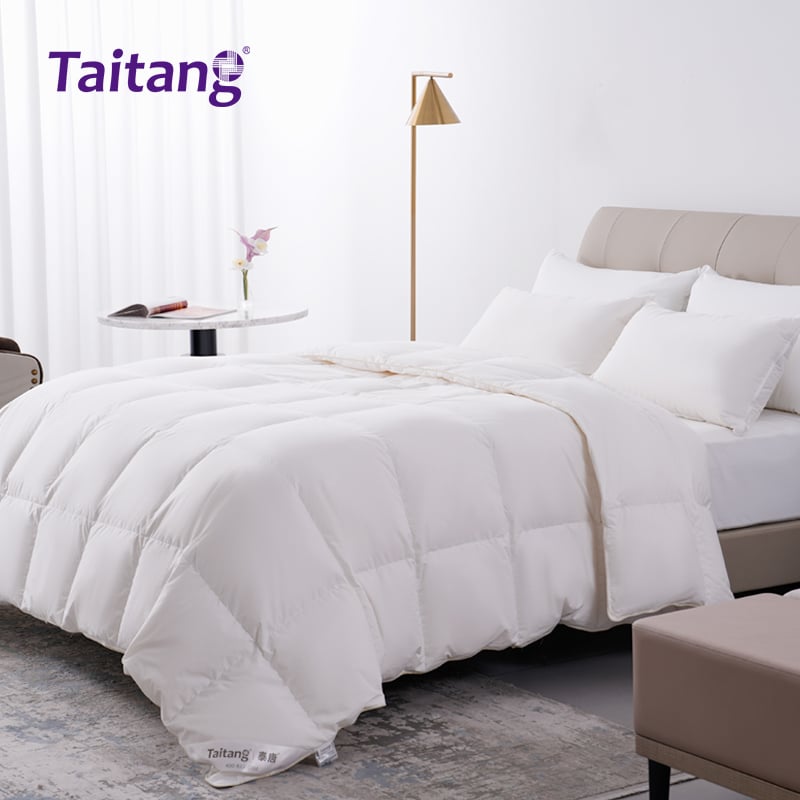 Side view of a hotel room with a high-end quilted down comforter, decorative pillows, and a bedside table.jpg