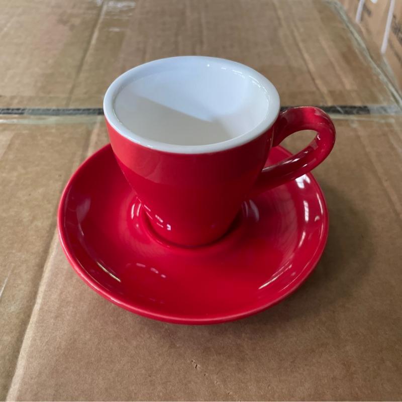 Vibrant red commercial ceramic coffee cup and matching saucer sample inspected on a shipping box.JPG