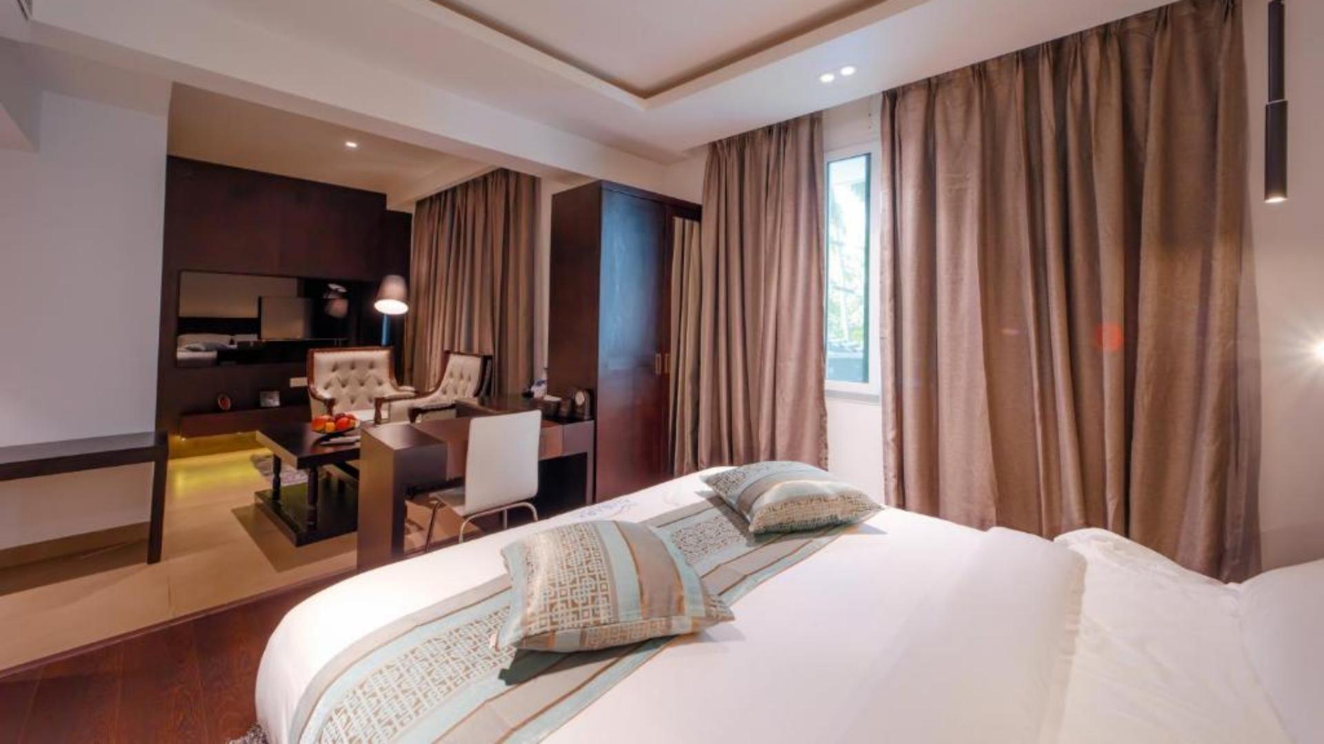 Modern hotel suite bedroom featuring a made bed with decorative pillows and elegant drapes at Ambara Suites.jpg