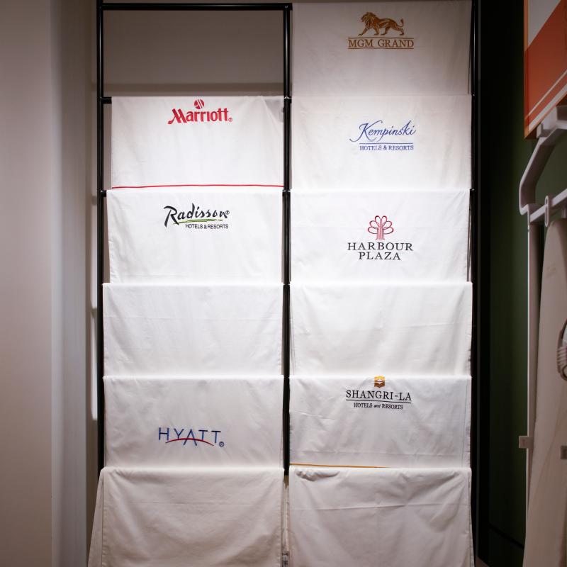 Custom embroidered white hotel bath towels featuring luxury brand logos displayed in Taitang hospitality showroom.JPG