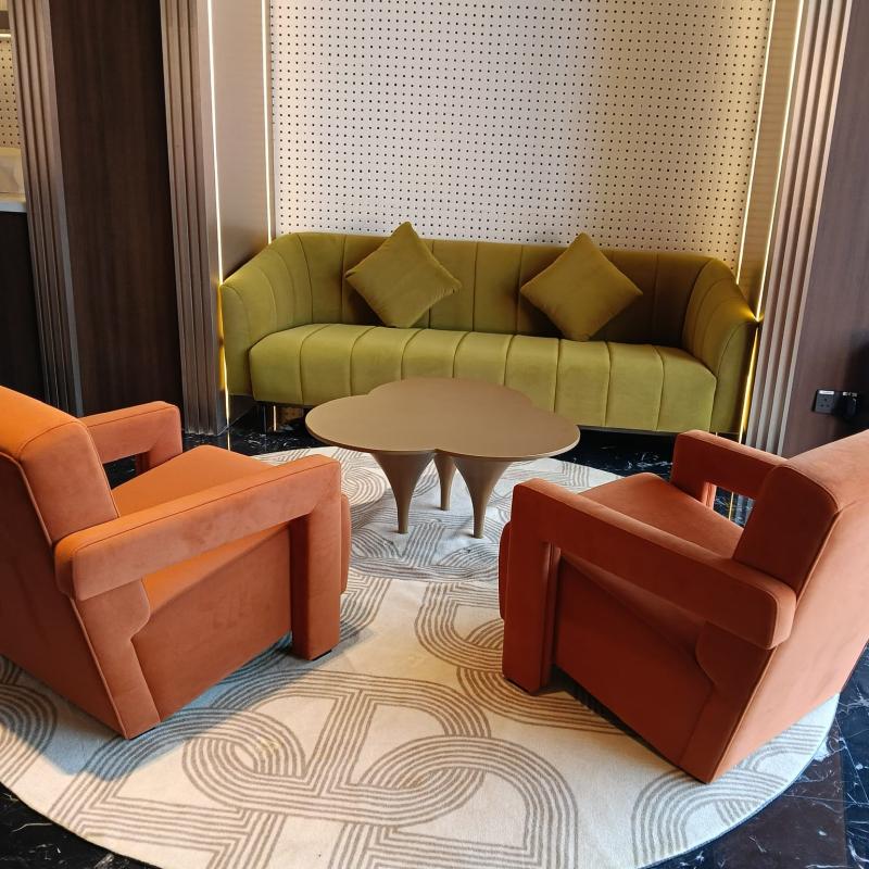 Hotel public lounge area featuring an avocado green sofa, two orange armchairs, and a modern coffee table.webp