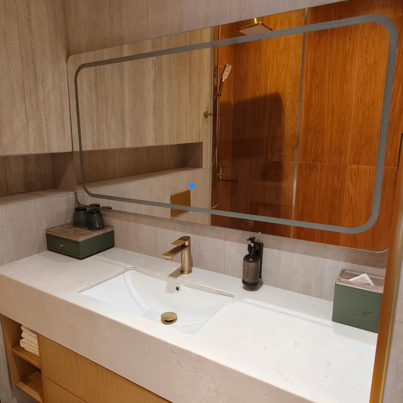 Modern hotel bathroom vanity counter with integrated white sink, illuminated mirror, and amenity dispensers.jpg