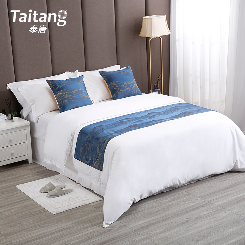 Taitang brand hotel bedroom setup featuring a white duvet set paired with blue patterned throw pillows and a matching bed runner.jpg