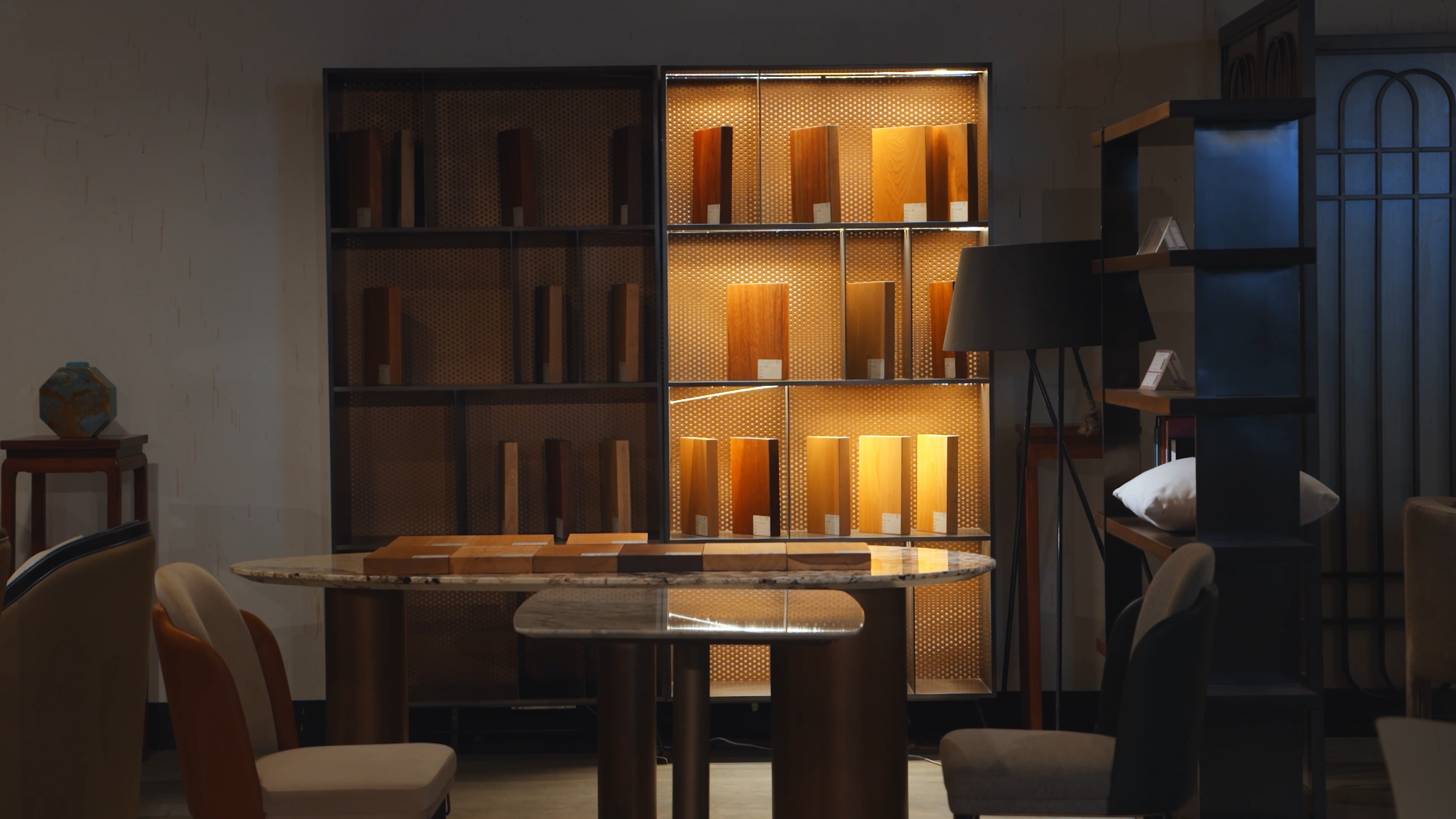 A professional material display area in a showroom, featuring backlit shelves with various wood finish samples, a marble-top table with swatches, and modern seating to showcase furniture customization options.