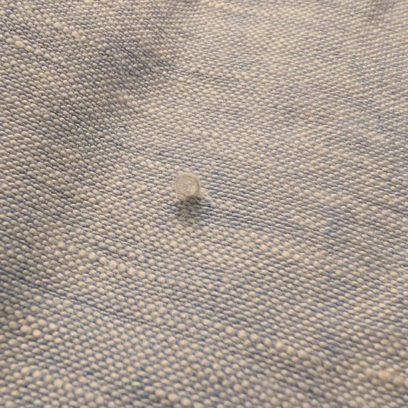 Close-up view of loose threads and snagging fabric surface on hotel bed sheets showing commercial laundry physical wear and tear.webp