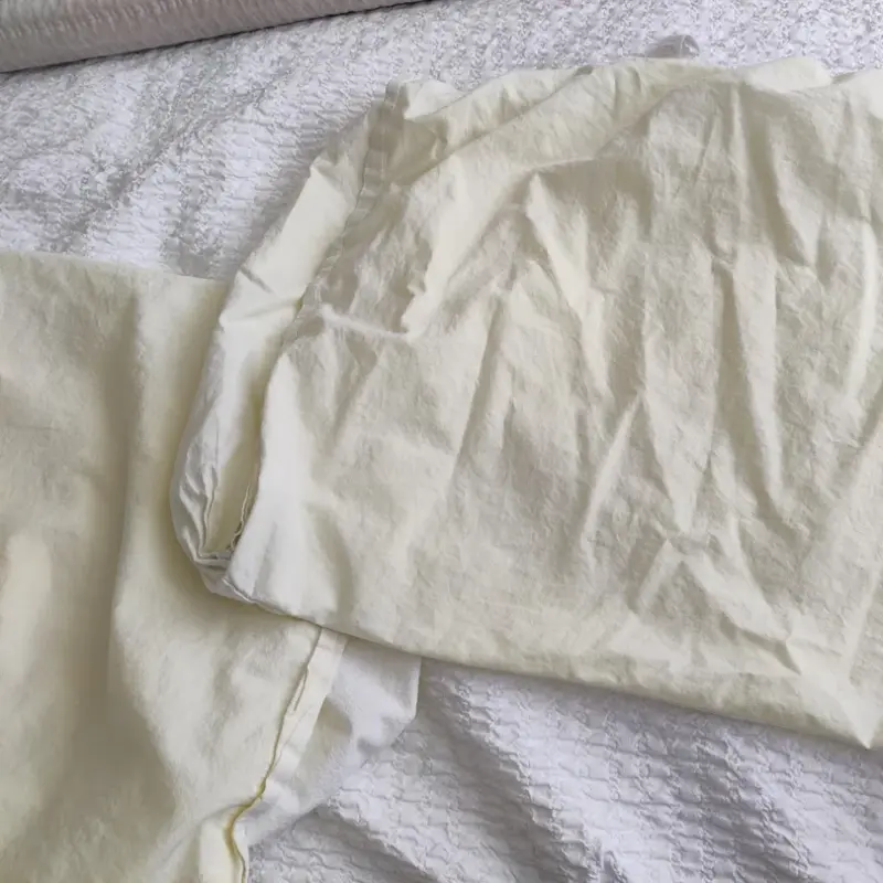 Yellowed and discolored white fitted bed sheets due to chemical residue oxidation and incorrect wash temperature in commercial laundering.webp