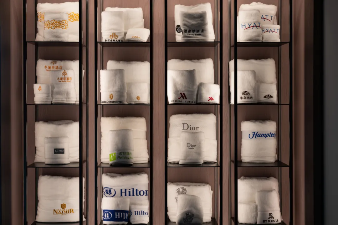 Wall of customized hotel towels and bathrobes featuring embroidered logos for global brands like Hilton, Marriott, and Hyatt.