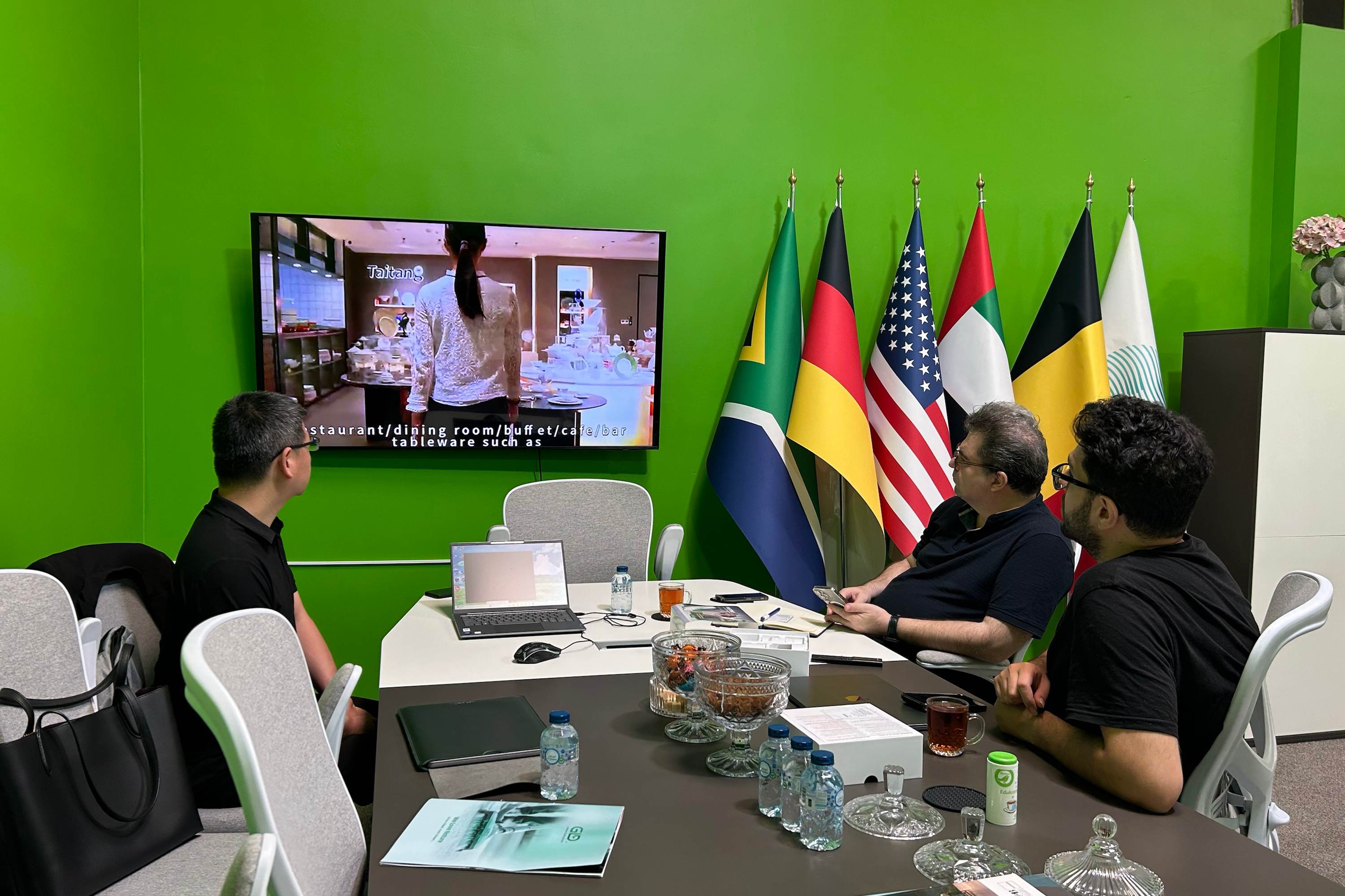 A professional business meeting between TAITANG experts and international clients, discussing global hotel supply chain strategies with multiple national flags in the background.