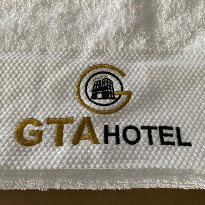 Plush white combed cotton hotel bath towel featuring a high-density gold and black embroidered GTA HOTEL logo.JPG