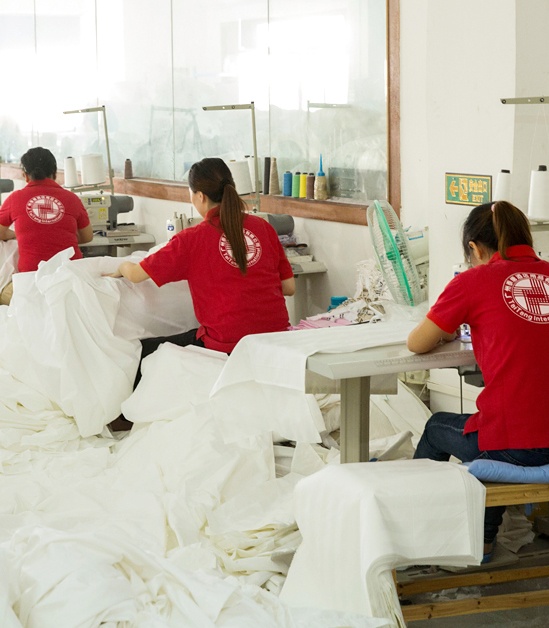 Professional textile workers in red uniforms meticulously sewing and quality-checking white hotel linens in a TAITANG manufacturing facility.
